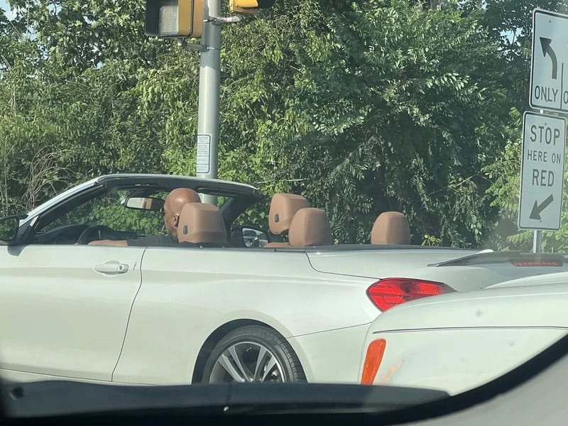 White convertible car with tan interior and no driver, parked near a stop sign.