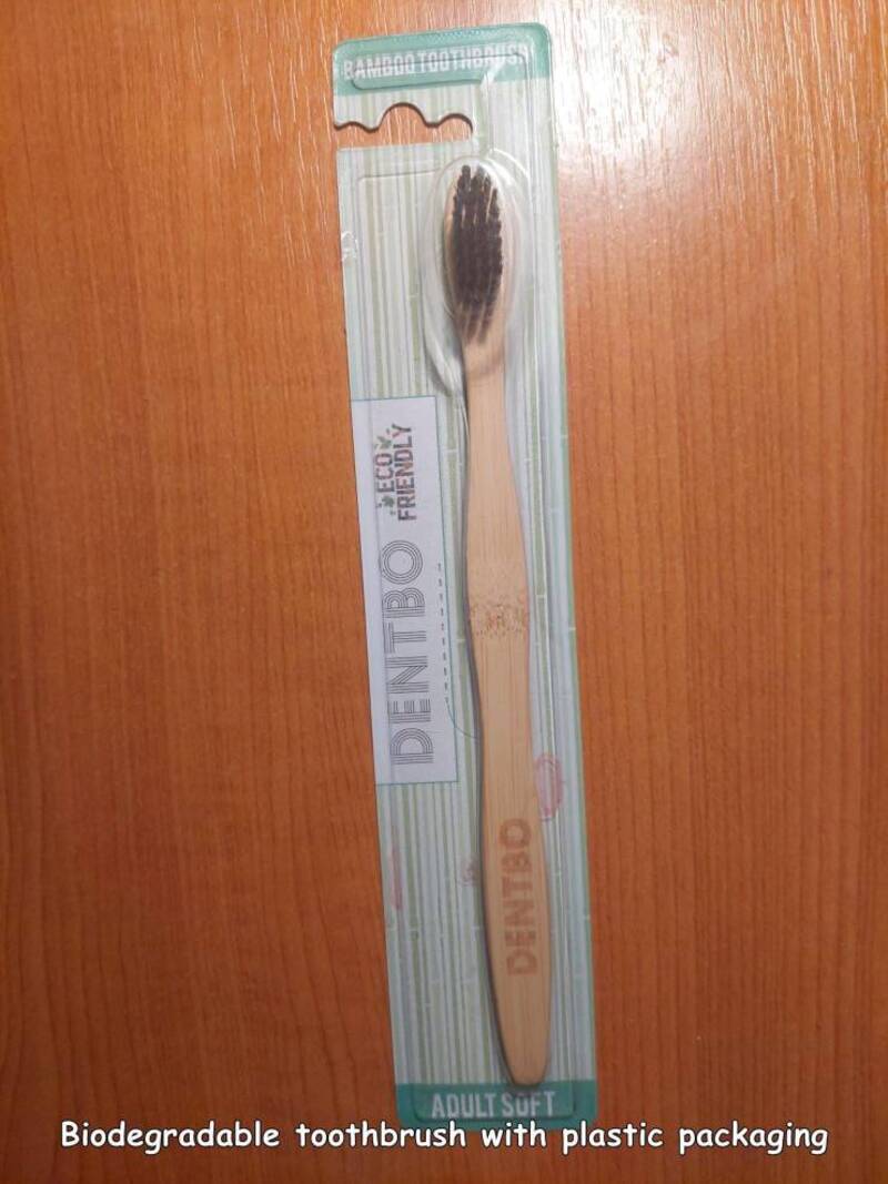 Biodegradable toothbrush with plastic packaging on wooden surface.