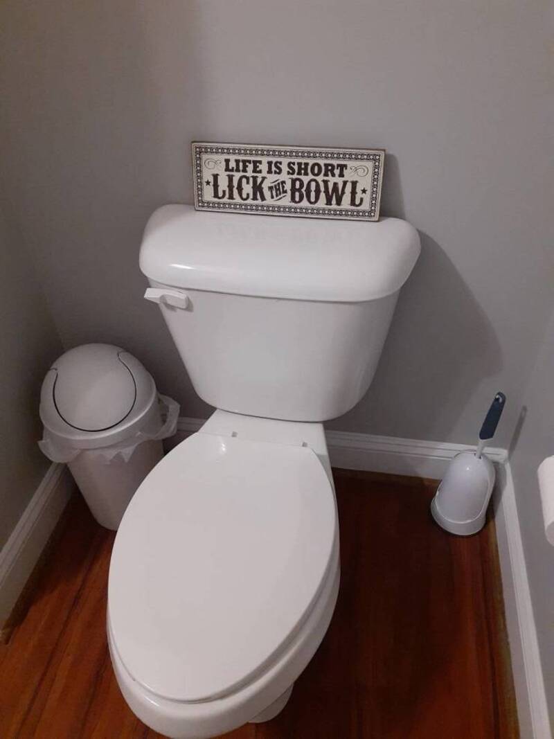 Toilet with a sign that says 'Life is short, lick the bowl' on top.