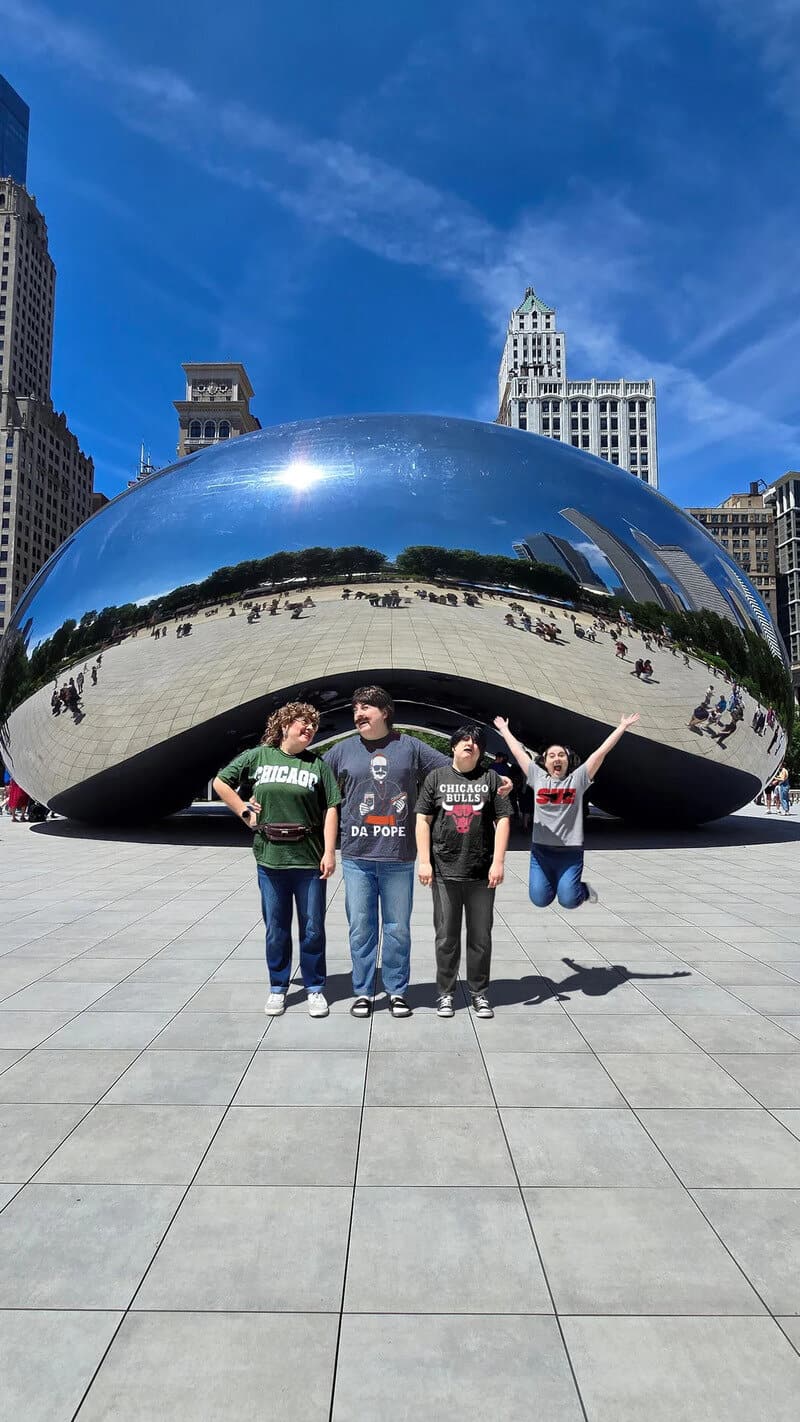 Four people in front of Cloud Gate sculpture in Chicago, with a jumping person on the right.