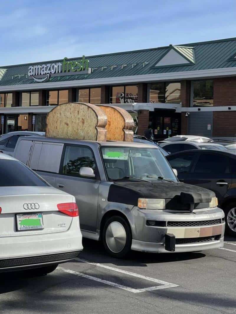 Car with a giant loaf of bread on its roof in front of Amazon Fresh.