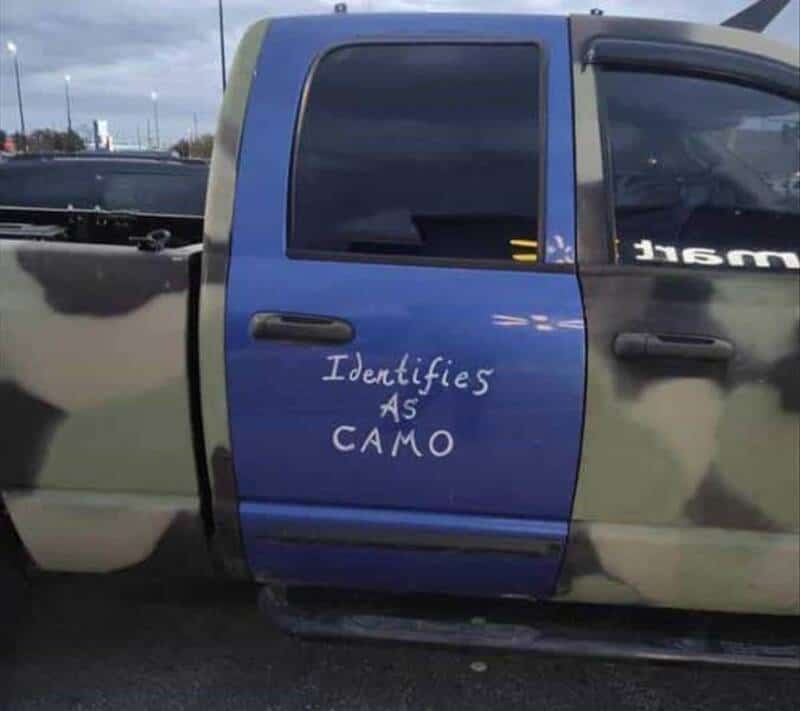 Truck with camouflage paint and a blue door that says 'Identifies as CAMO'.