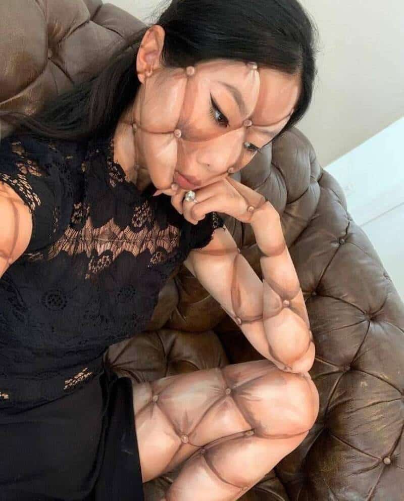 Woman with distorted face and body sitting on a brown leather couch.