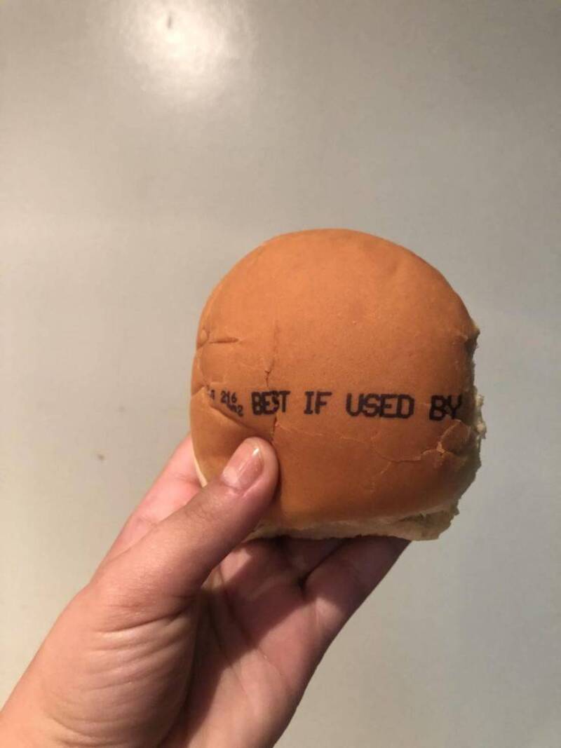 A hand holding a burger bun with a label that says 'BEST IF USED BY'.