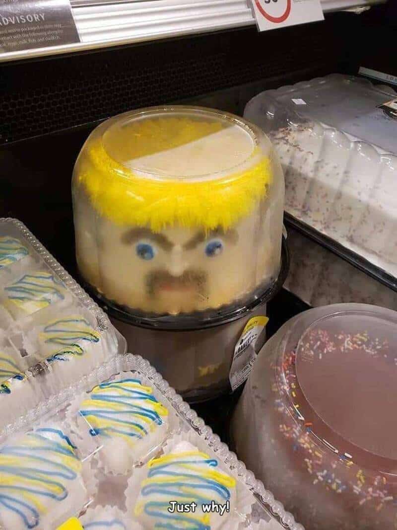 Cake with a face and yellow hair inside a plastic container on a store shelf.