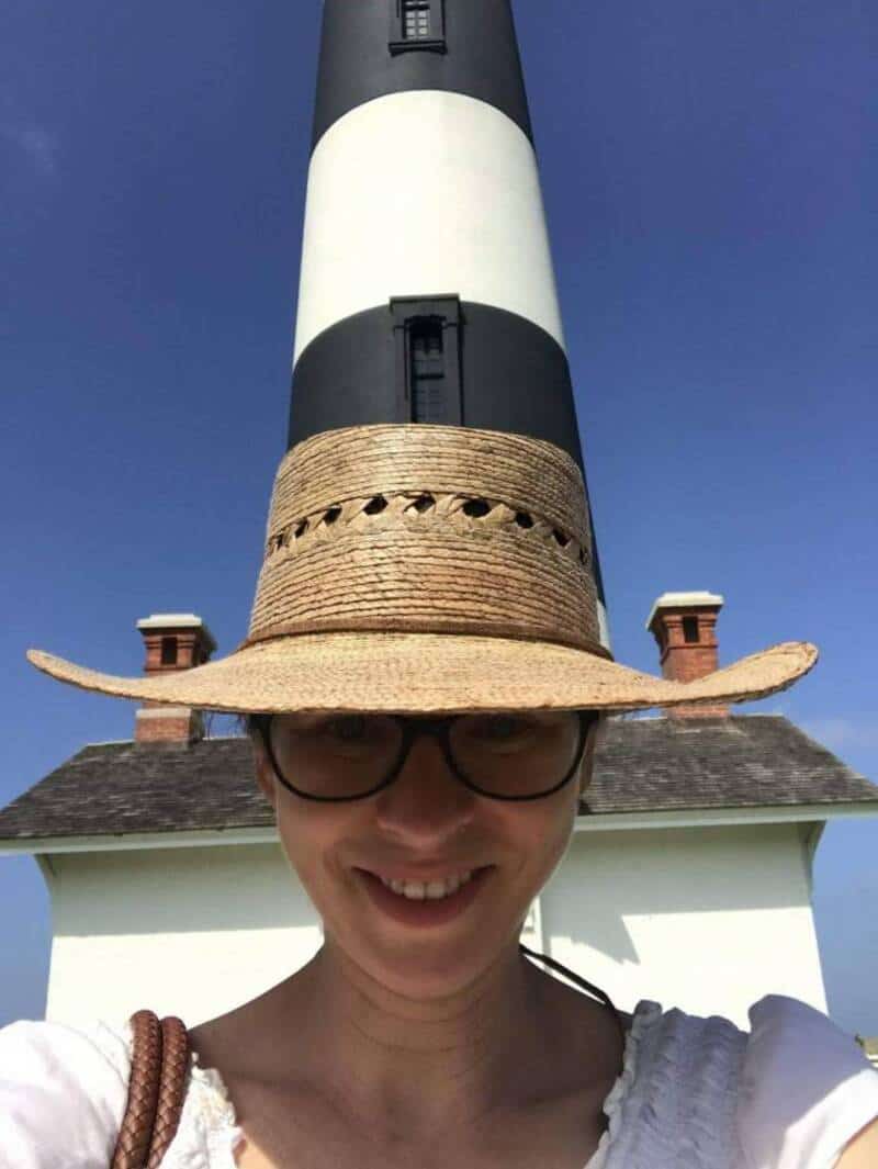 Person wearing a straw hat with a lighthouse on their head, smiling.