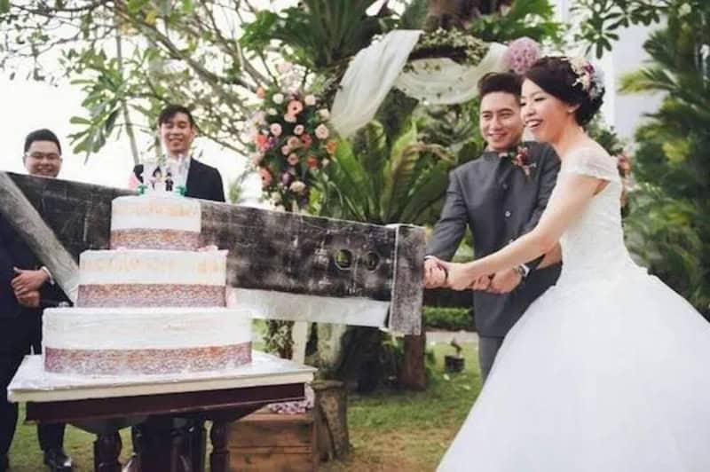 Wedding couple cutting cake outdoors with friends and floral decorations.