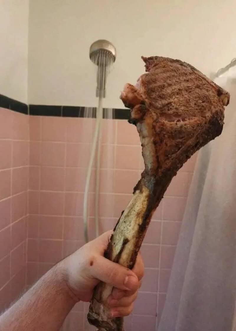 Hand holding a large cooked meat bone in a bathroom shower.
