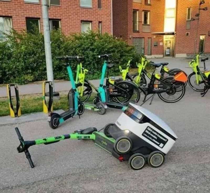 E-scooter and e-bike sharing station with a delivery robot on the street.