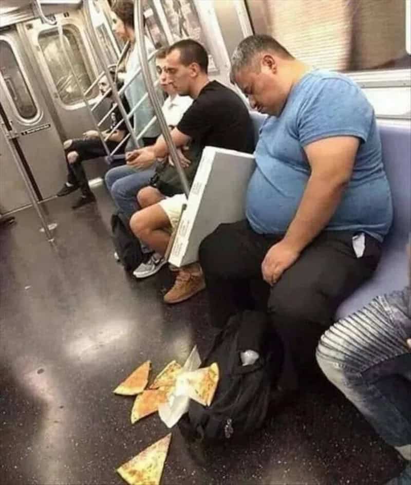 Man sleeping on subway with pizza slices on the floor in front of him.