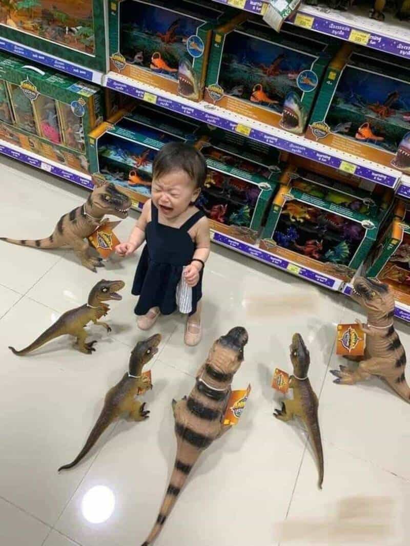 A young child crying while surrounded by toy dinosaurs in a store aisle.