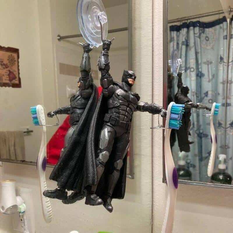 Batman action figure hanging from a mirror with toothbrushes in the background.