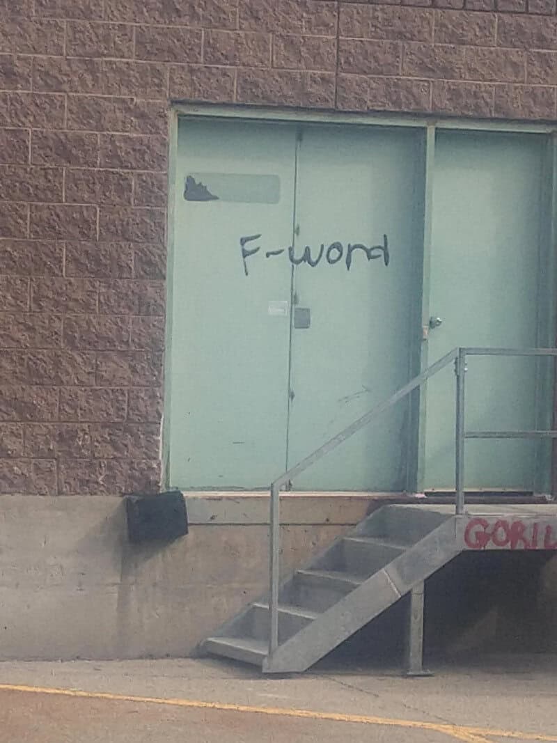 F-word graffiti on a green door with stairs and a railing outside.