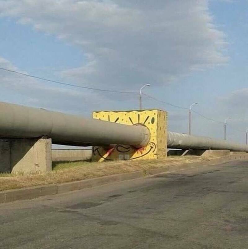 Large pipe broken through a yellow concrete barrier on the roadside.