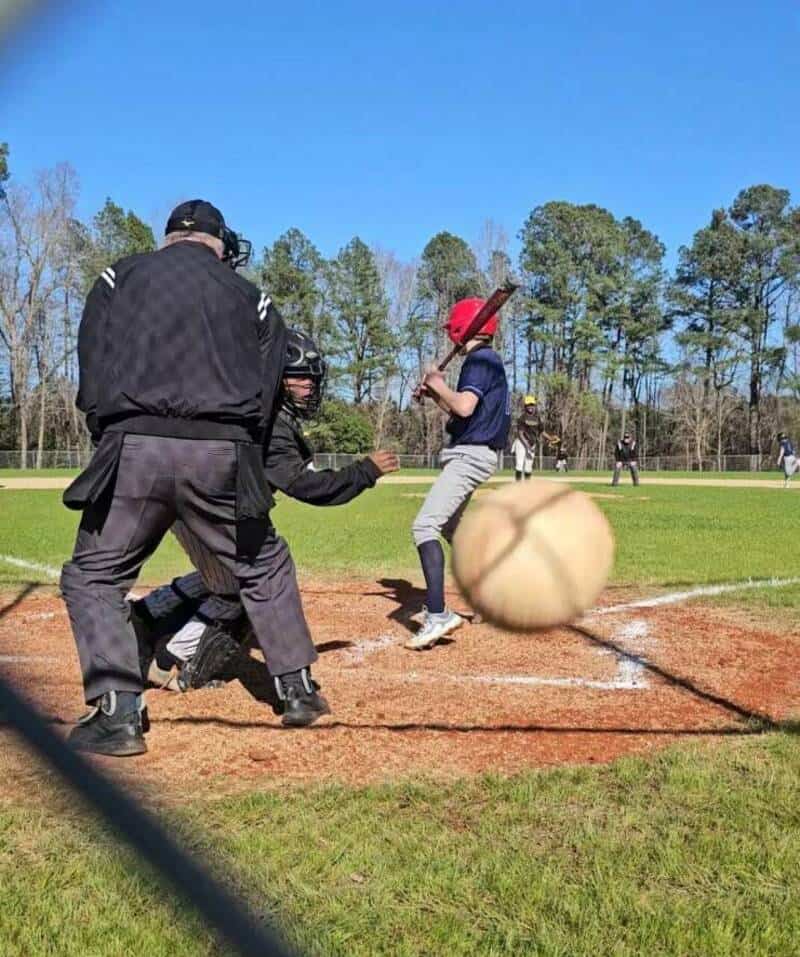 Young baseball player swinging at a pitch during a game on a sunny day.