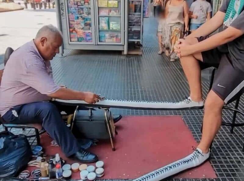 Elderly man playing a musical instrument on the street with a crowd nearby.