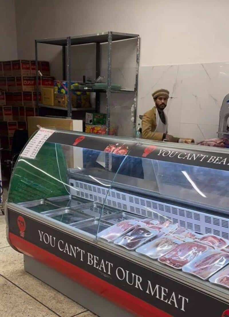 Meat display case with packages of meat and a man in the background.