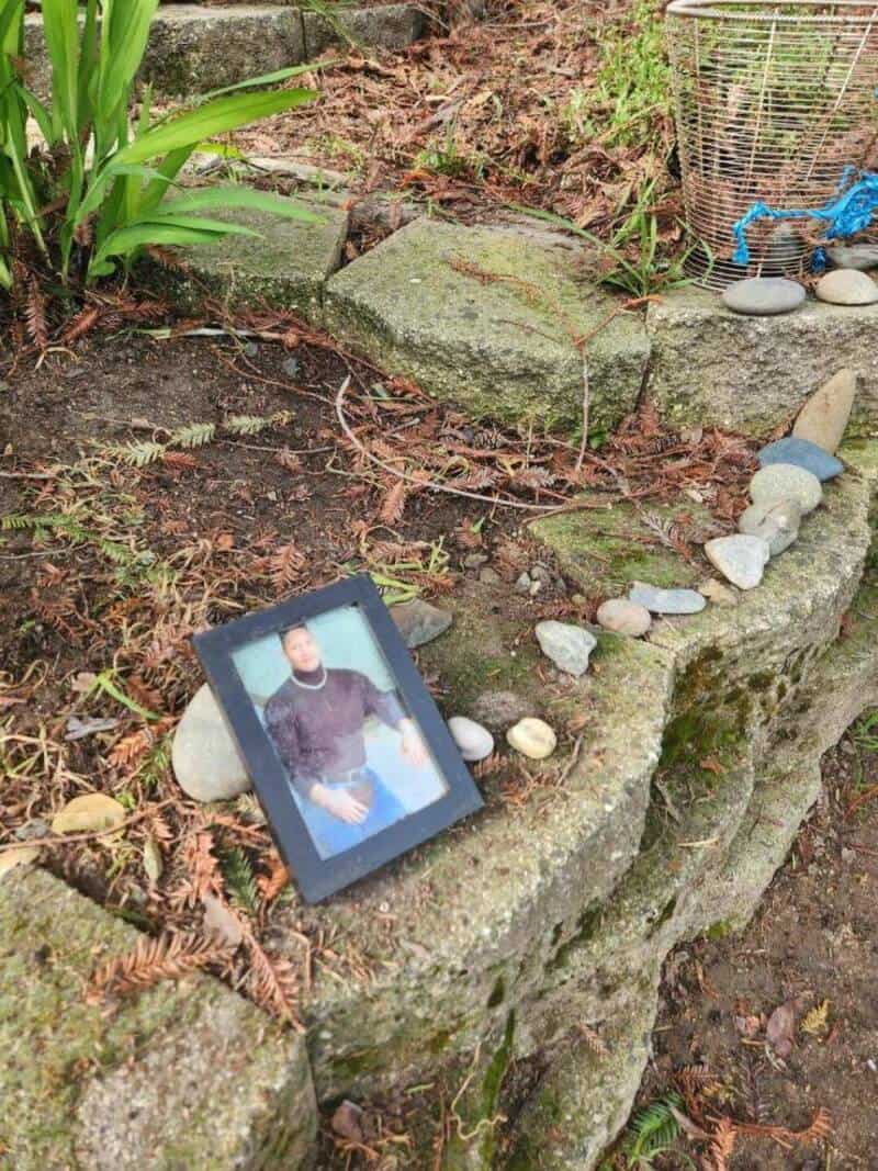 Framed photo of a person placed on a stone wall outdoors with plants and rocks around.