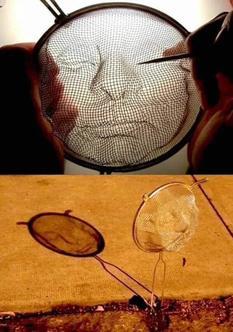 Artistic wire mesh face sculpture with glasses and a wooden surface background.