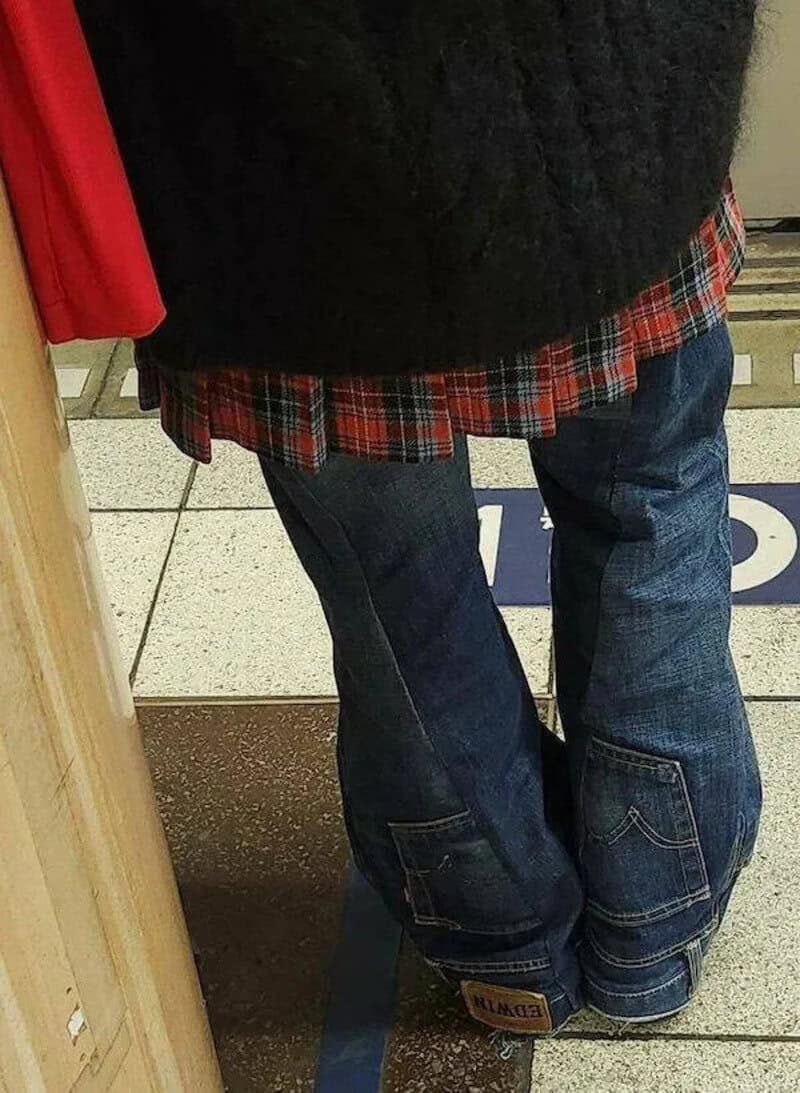 A person wearing baggy jeans and a black sweater, standing on a tiled floor.