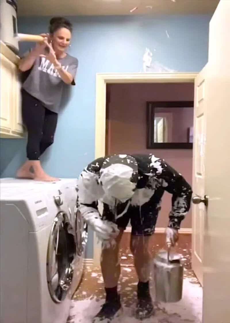 Woman and man having fun with foam in laundry room, playful scene.