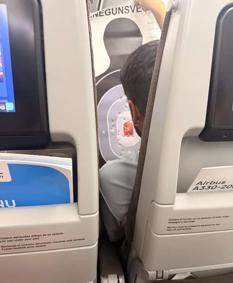 Passenger sitting in airplane seat with a safety instruction poster in the background.