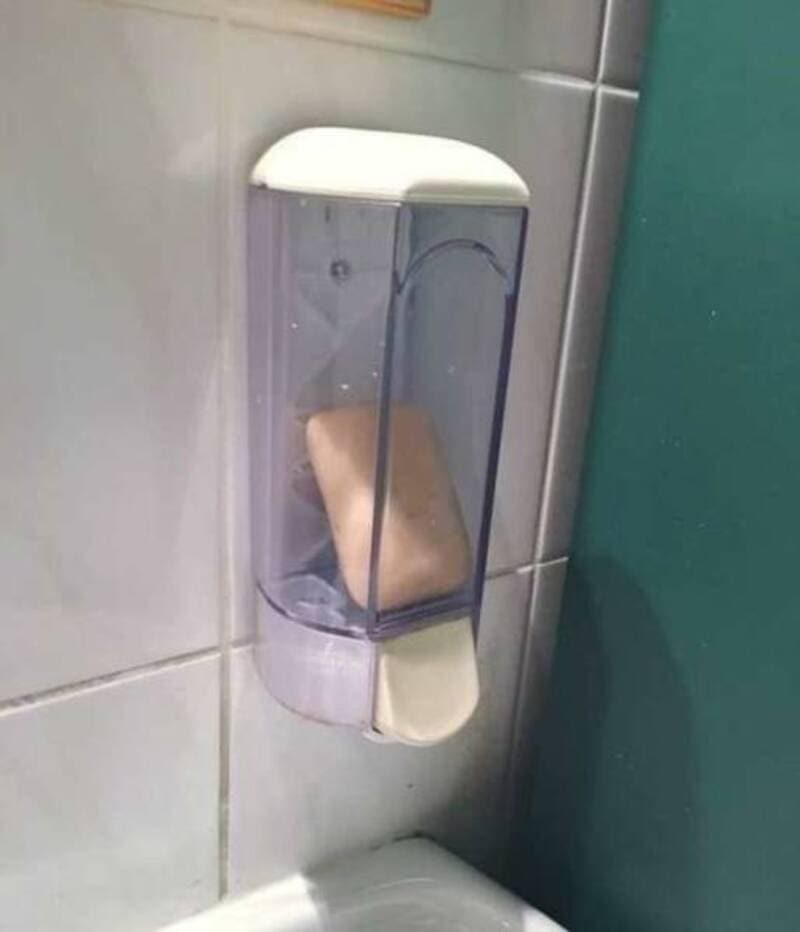 Soap dispenser with a bar of soap inside, mounted on tiled wall.