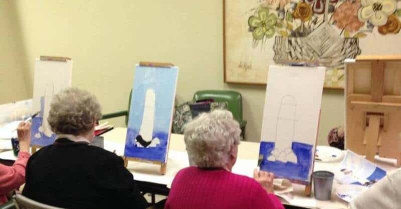 Seniors painting seascape in an art class with easels and canvases.