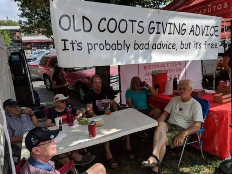 OLD COOTS GIVING ADVICE sign, group of seniors sitting at a table outdoors.