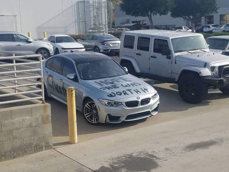 BMW car with protest message on hood, parked in lot with other vehicles.