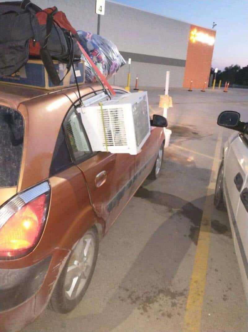 Car with luggage and air conditioner on roof in parking lot at dusk.