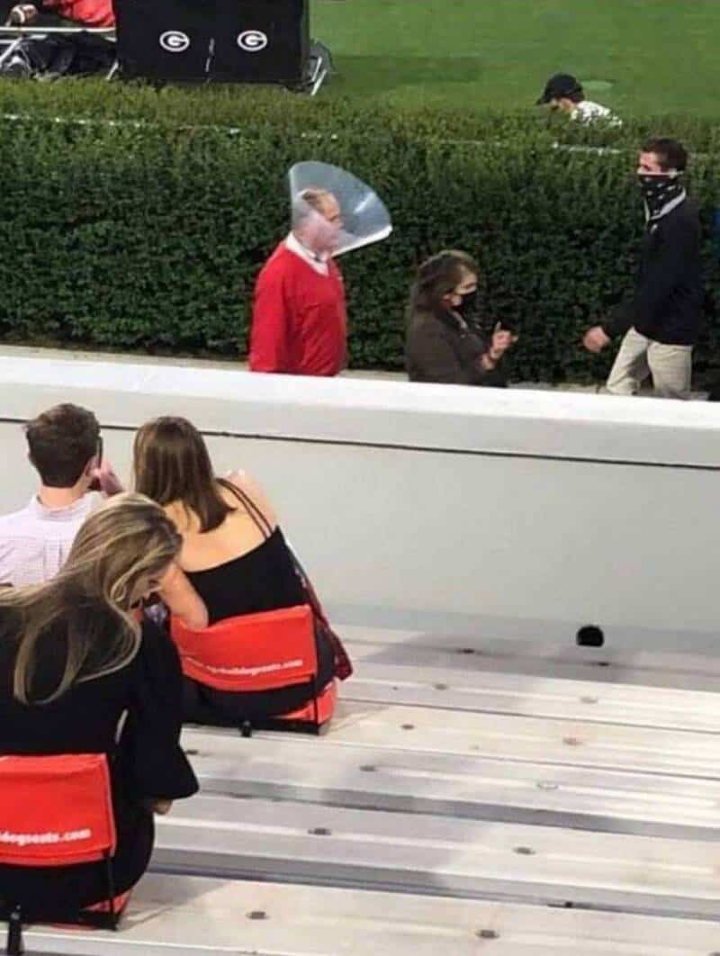 A woman with a face shield talking to a man and a woman wearing masks outdoors.