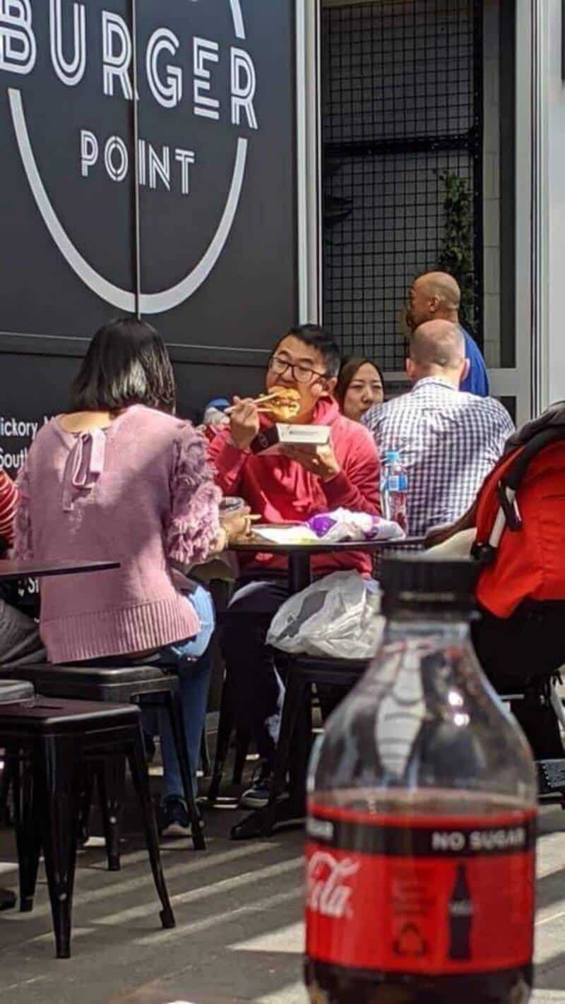 A person in a red jacket eating a burger at a burger point outdoor seating area.