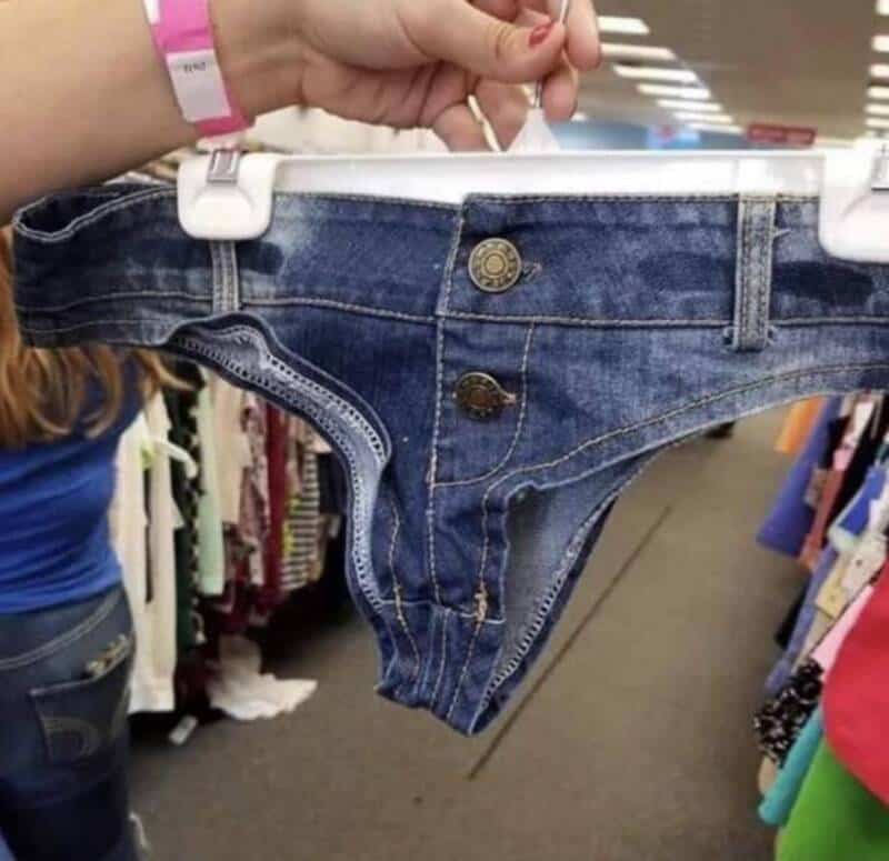 Woman holding a pair of tiny denim shorts in a store aisle.