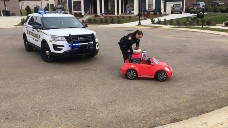 A police officer inspecting a small red toy car in an open parking lot.