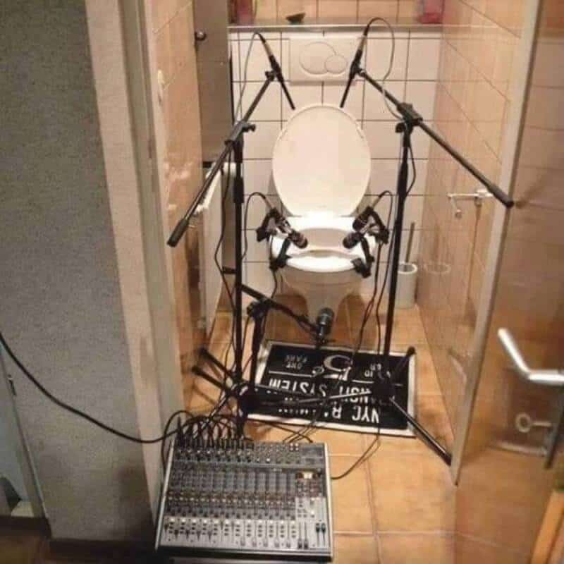 A person recording audio of a toilet with multiple microphones and a sound mixer in a small bathroom.