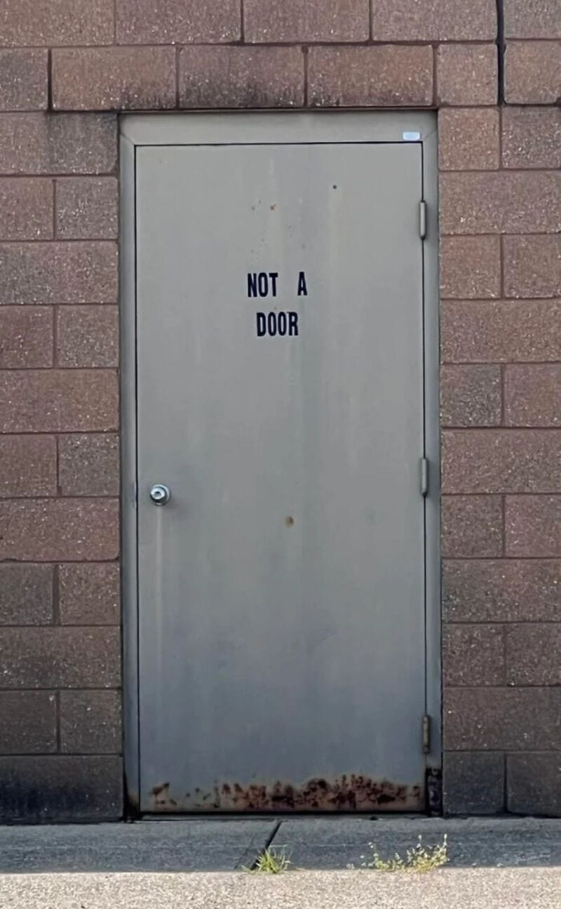 NOT A DOOR - Metal door with rust at the bottom, set in a brick wall.