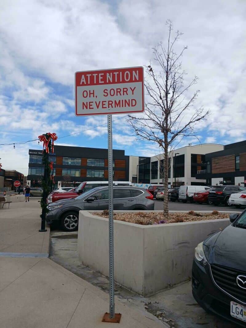 Attention sign reading "OH, SORRY NEVERMIND" in a parking lot.