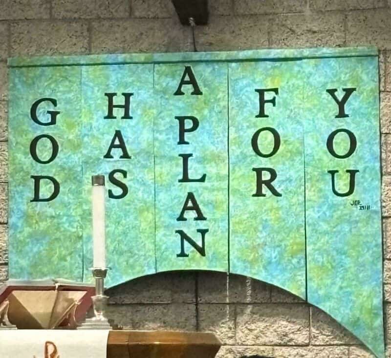 Sign reads 'GOD HAS A PLAN FOR YOU' on a green background with black letters.