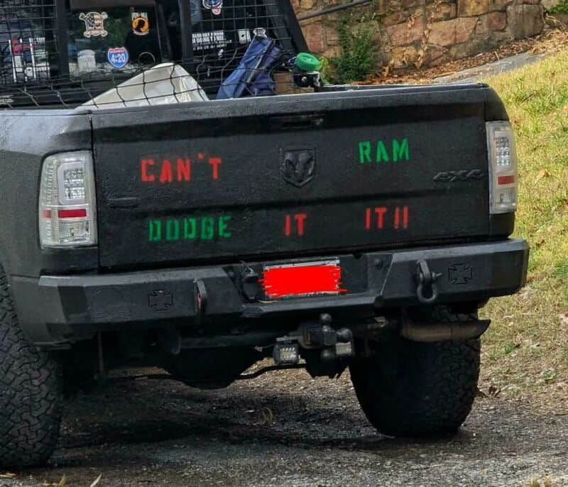 Truck with a sign that says 'CAN'T RAM DODGE IT' on the tailgate.
