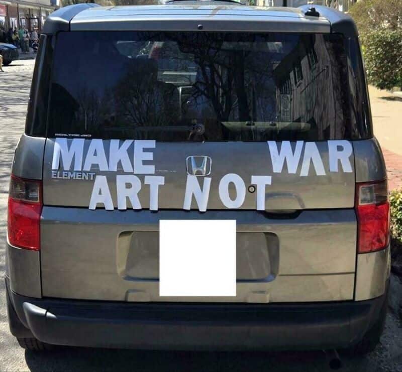 Car with a sign on the back that says 'MAKE ART NOT WAR'.