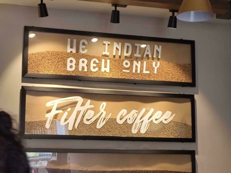 Sign reads 'The Indian Brew Only Filter Coffee' with a background of coffee beans.