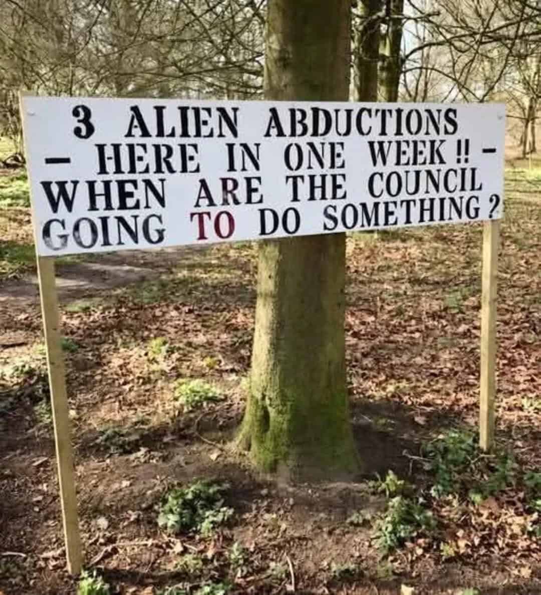 Sign about alien abductions and council action in a forest setting.