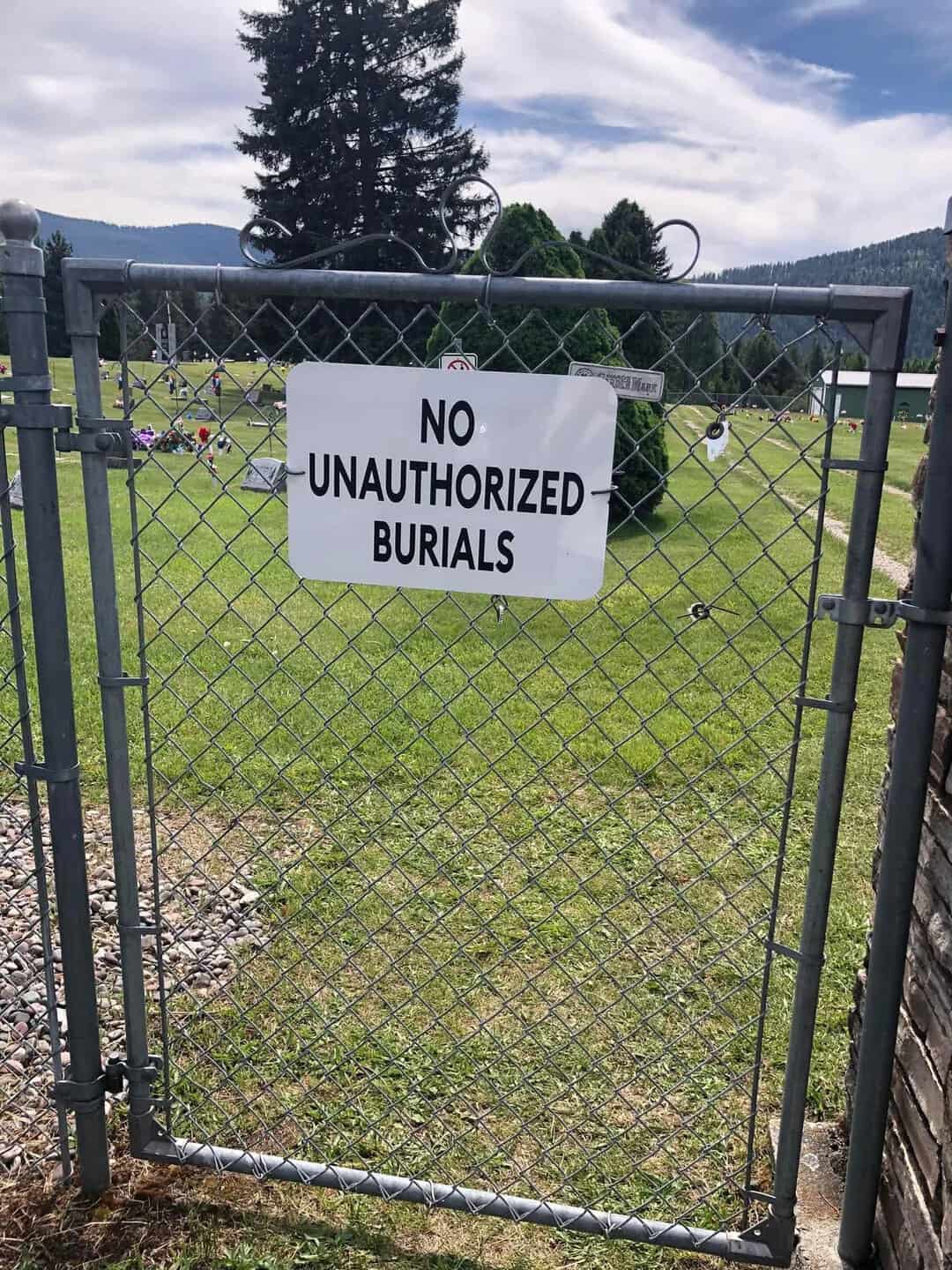 Sign on gate reads 'NO UNAUTHORIZED BURIALS' in a cemetery.