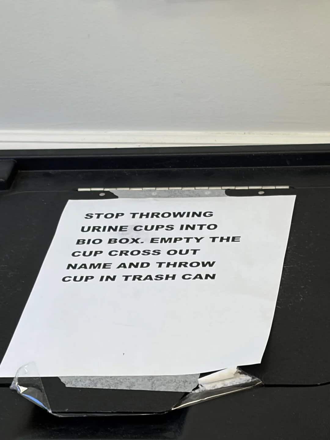 Sign instructs to stop throwing urine cups into bio box and to throw cups in trash can.