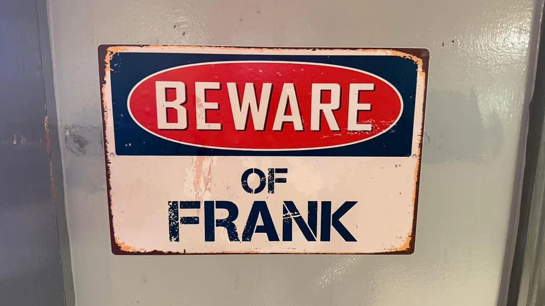 Beware of Frank sign with rust and worn paint on a wall.