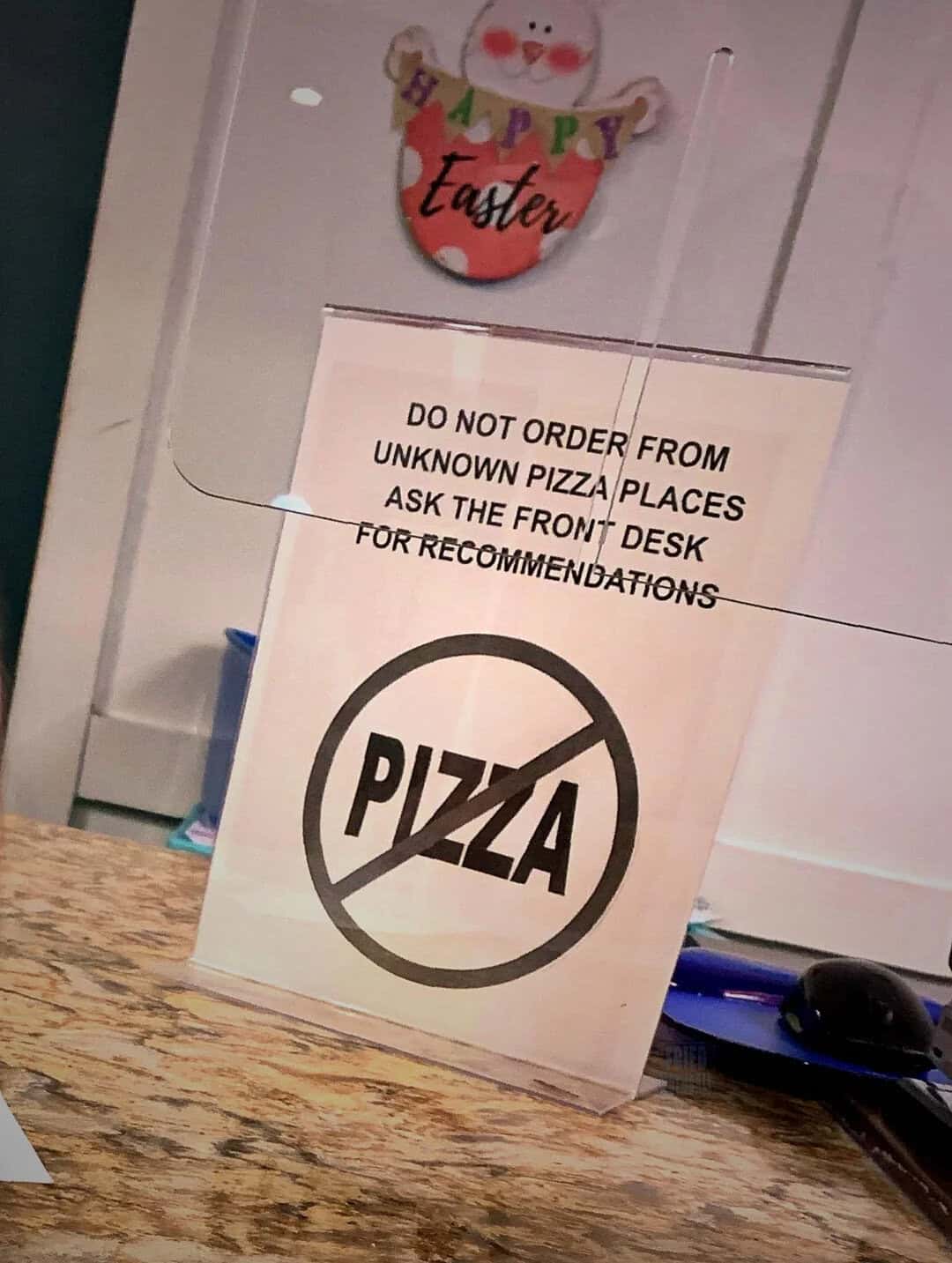 Sign says 'Do not order from unknown pizza places, ask the front desk for recommendations' with a 'P.