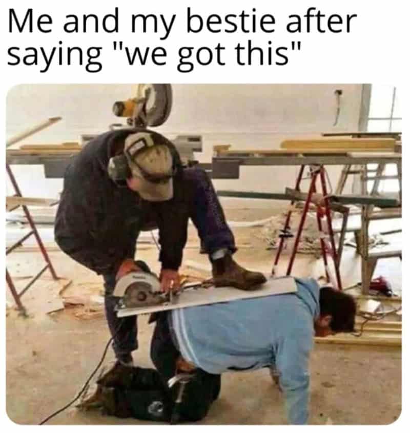 Two men in a workshop, one cutting wood while the other is on all fours.