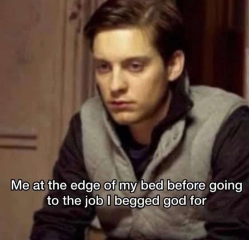 Young man with a serious expression, wearing a gray and black hoodie, sitting indoors.