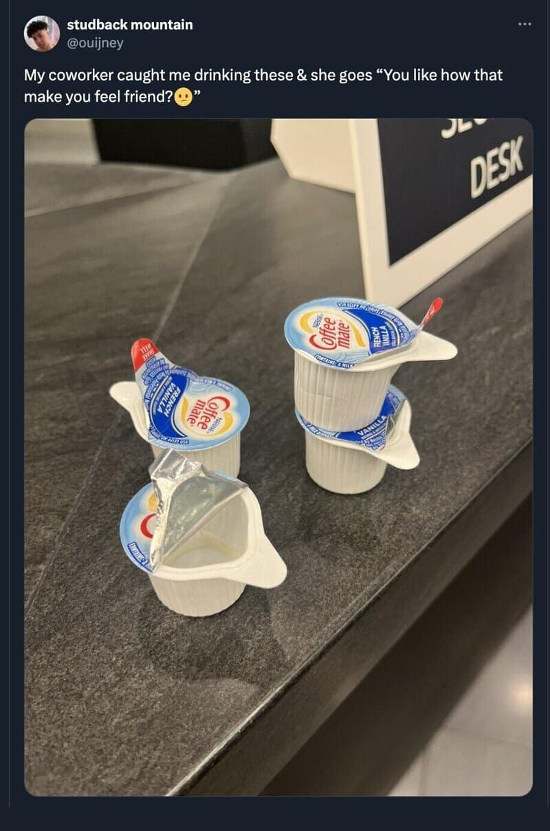 Two yogurt cups with foil lids and spoons on a desk, one with a spoon inside.